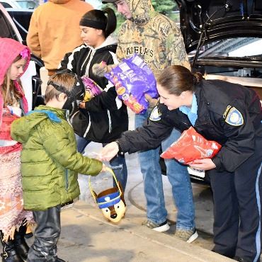 Police giving candy to costumed children during a trunk or treat.